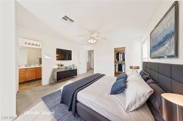 bedroom with light carpet, a walk in closet, ceiling fan, connected bathroom, and a closet