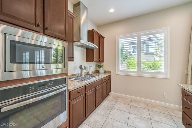 kitchen featuring light stone countertops, light tile patterned flooring, wall chimney range hood, and appliances with stainless steel finishes