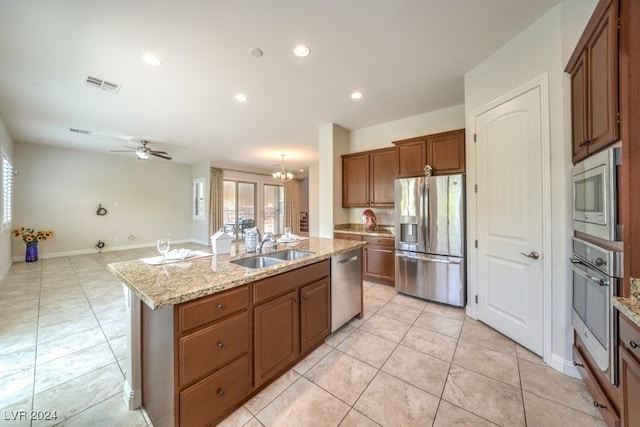 kitchen featuring light stone countertops, ceiling fan with notable chandelier, stainless steel appliances, sink, and a center island with sink