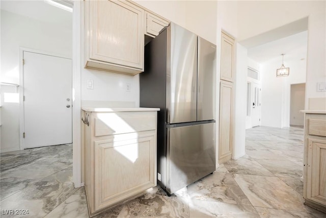 kitchen featuring stainless steel refrigerator, light brown cabinetry, and pendant lighting