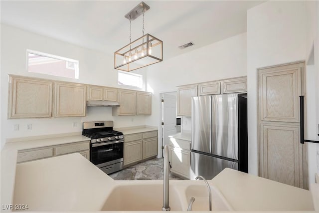 kitchen with appliances with stainless steel finishes, a towering ceiling, hanging light fixtures, and light brown cabinetry