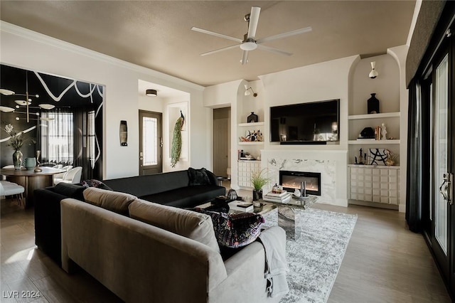 living room featuring built in shelves, ceiling fan, a premium fireplace, and light hardwood / wood-style flooring