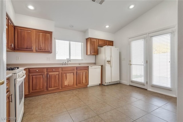 kitchen featuring a healthy amount of sunlight, white appliances, light tile patterned floors, and vaulted ceiling