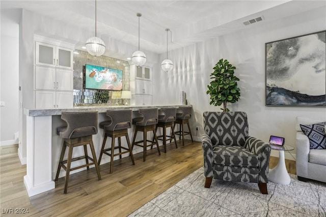 bar with a notable chandelier, light hardwood / wood-style floors, white cabinetry, and hanging light fixtures