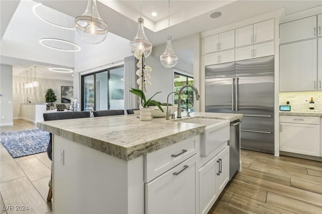 kitchen with white cabinetry, built in fridge, sink, and an island with sink