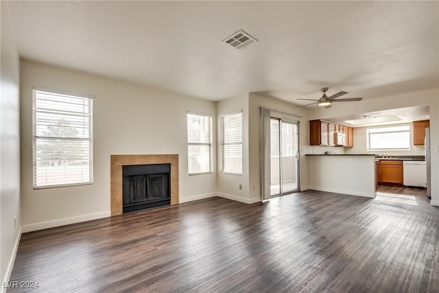 unfurnished living room with ceiling fan, dark wood-type flooring, and a tiled fireplace