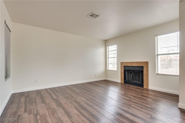 unfurnished living room featuring dark hardwood / wood-style flooring and a tiled fireplace