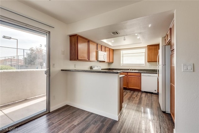 kitchen featuring sink, a raised ceiling, white appliances, and dark wood-type flooring