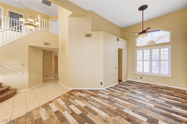 spare room with light hardwood / wood-style floors, a towering ceiling, and ceiling fan with notable chandelier