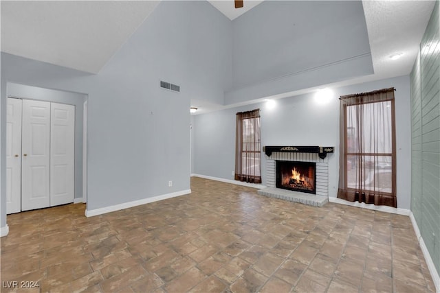 unfurnished living room featuring a towering ceiling and a brick fireplace