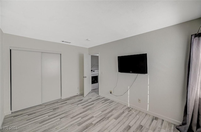 unfurnished bedroom featuring washer / dryer, light hardwood / wood-style flooring, and a closet