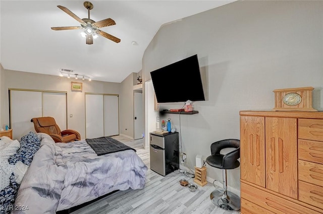 bedroom featuring two closets, light hardwood / wood-style flooring, ceiling fan, and lofted ceiling