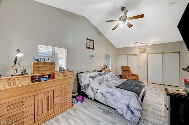 bedroom featuring multiple closets, ceiling fan, lofted ceiling, and light wood-type flooring