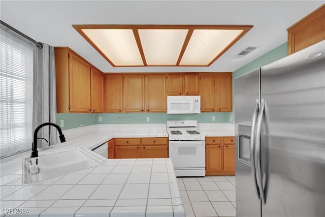 kitchen featuring sink, kitchen peninsula, tile countertops, white appliances, and light tile patterned floors