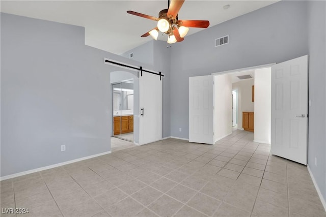 tiled spare room featuring a barn door, ceiling fan, and high vaulted ceiling