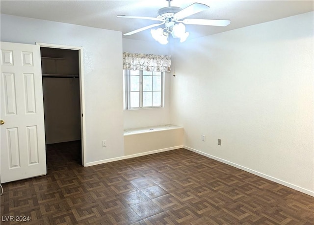 unfurnished bedroom featuring a closet, a walk in closet, ceiling fan, and dark parquet flooring