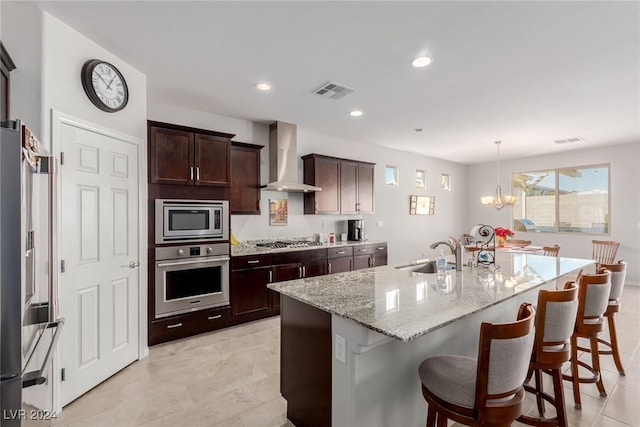 kitchen with sink, wall chimney exhaust hood, stainless steel appliances, an island with sink, and a breakfast bar area