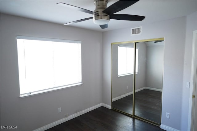 unfurnished bedroom with multiple windows, dark wood-type flooring, ceiling fan, and a closet