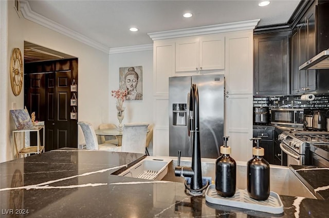 kitchen featuring white cabinetry, wall chimney exhaust hood, stainless steel appliances, dark stone counters, and ornamental molding