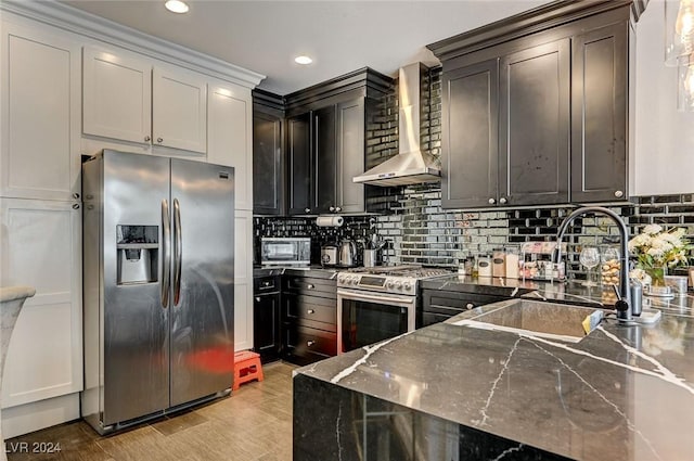 kitchen featuring sink, wall chimney exhaust hood, tasteful backsplash, light hardwood / wood-style flooring, and appliances with stainless steel finishes