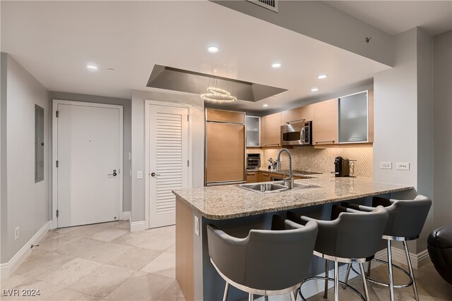 kitchen with kitchen peninsula, a kitchen breakfast bar, decorative backsplash, light stone countertops, and built in fridge