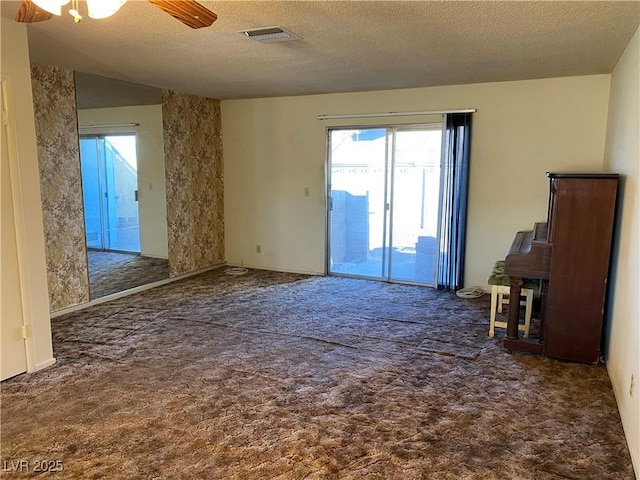 spare room with ceiling fan, a textured ceiling, and dark colored carpet