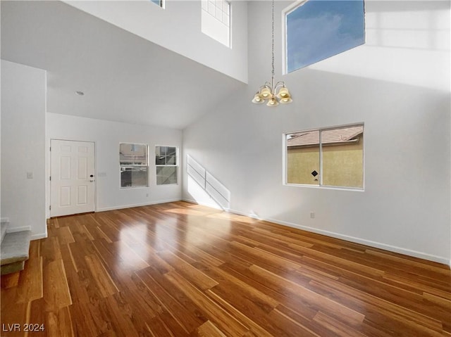 unfurnished living room featuring a towering ceiling, wood-type flooring, a wealth of natural light, and an inviting chandelier