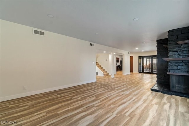 unfurnished living room with a stone fireplace and light wood-type flooring