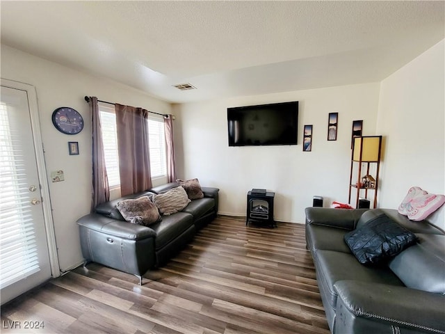 living room featuring visible vents, a textured ceiling, wood finished floors, and a wood stove