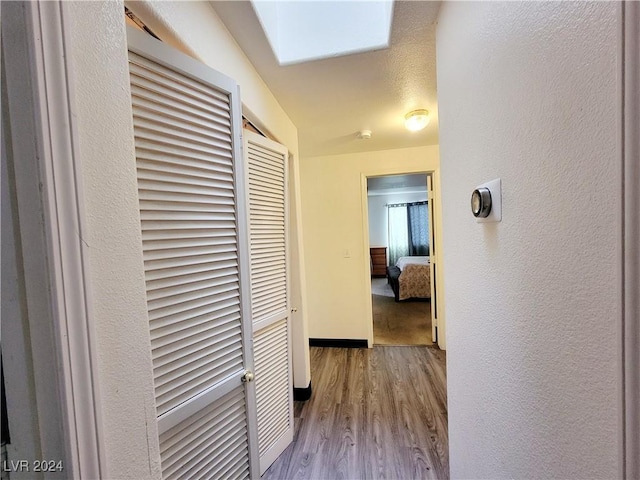 hallway with a skylight, a textured wall, baseboards, and wood finished floors