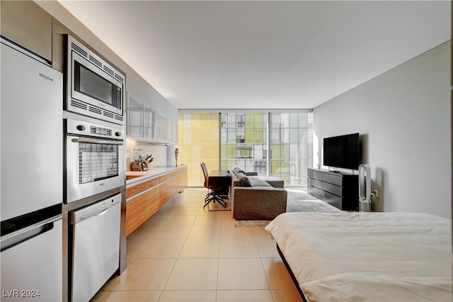 bedroom featuring white fridge, a wall of windows, and light tile patterned floors