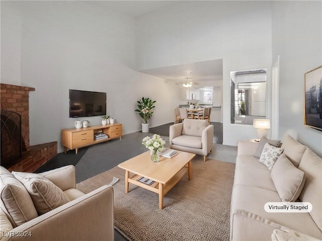 living room featuring ceiling fan, a fireplace, and a high ceiling