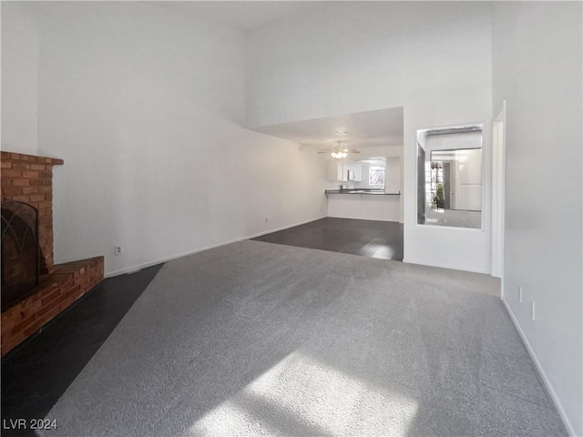 living room featuring dark colored carpet, a towering ceiling, a brick fireplace, and ceiling fan