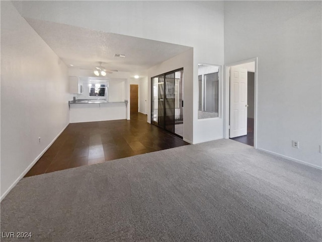 unfurnished living room with a textured ceiling, dark carpet, and ceiling fan