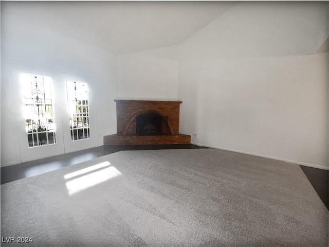 unfurnished living room featuring dark colored carpet, vaulted ceiling, and a brick fireplace