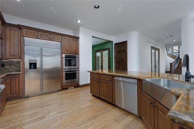 kitchen with light stone countertops, sink, stainless steel appliances, and light hardwood / wood-style floors