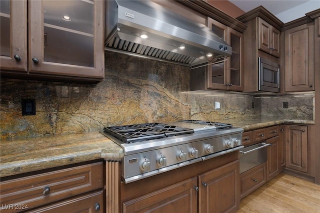 kitchen with wall chimney exhaust hood, light stone countertops, stainless steel appliances, and tasteful backsplash