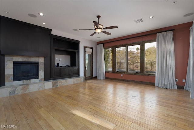 unfurnished living room featuring a tile fireplace, ceiling fan, and light wood-type flooring