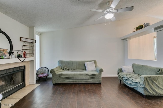 living room featuring a tiled fireplace, hardwood / wood-style floors, a textured ceiling, and ceiling fan