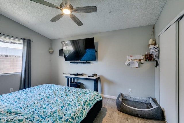 bedroom with ceiling fan, hardwood / wood-style floors, a textured ceiling, vaulted ceiling, and a closet