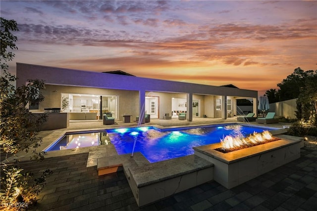 pool at dusk with exterior kitchen, a jacuzzi, pool water feature, an outdoor living space with a fire pit, and a patio area