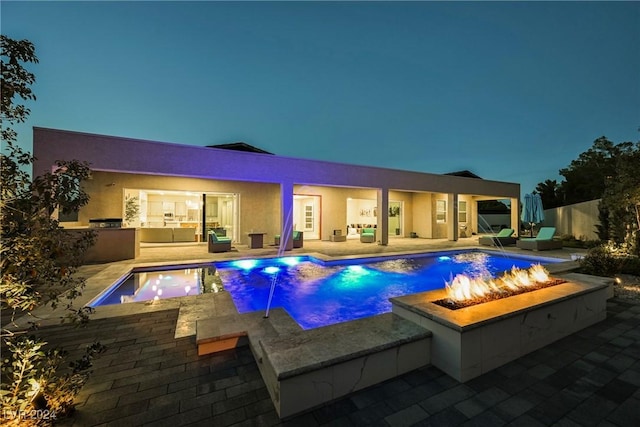 pool at dusk with a patio area, pool water feature, an outdoor living space with a fire pit, and a jacuzzi