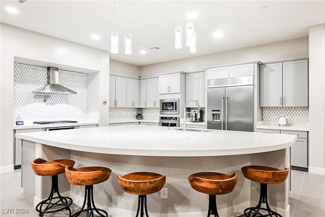 kitchen featuring wall chimney exhaust hood, backsplash, built in appliances, a spacious island, and light tile patterned floors