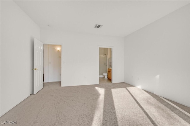 unfurnished bedroom featuring light carpet and ensuite bathroom