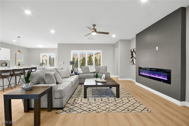 living room featuring light wood-type flooring, ceiling fan, and sink