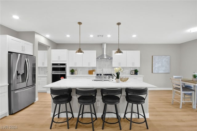 kitchen featuring tasteful backsplash, wall chimney exhaust hood, stainless steel appliances, pendant lighting, and an island with sink