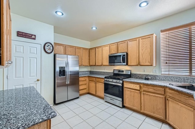 kitchen with sink, stainless steel appliances, dark stone counters, and light tile patterned flooring