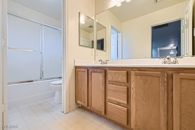 bathroom with double vanity, bath / shower combo with glass door, toilet, tile patterned floors, and a sink