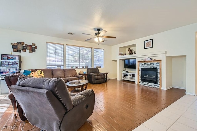 living room with visible vents, ceiling fan, wood finished floors, a tile fireplace, and baseboards