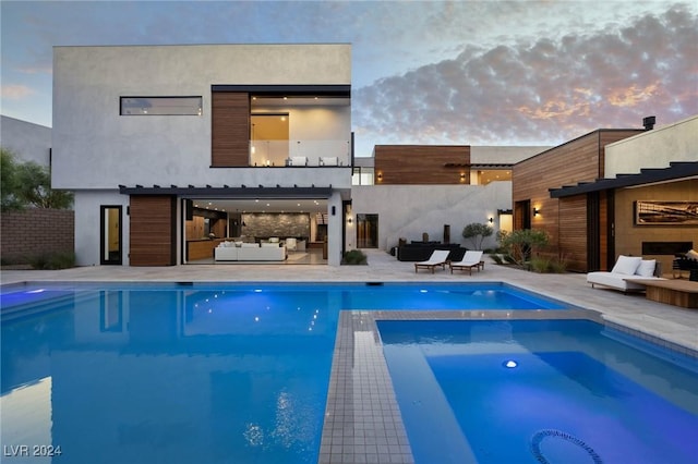 back house at dusk featuring a swimming pool with hot tub and a patio